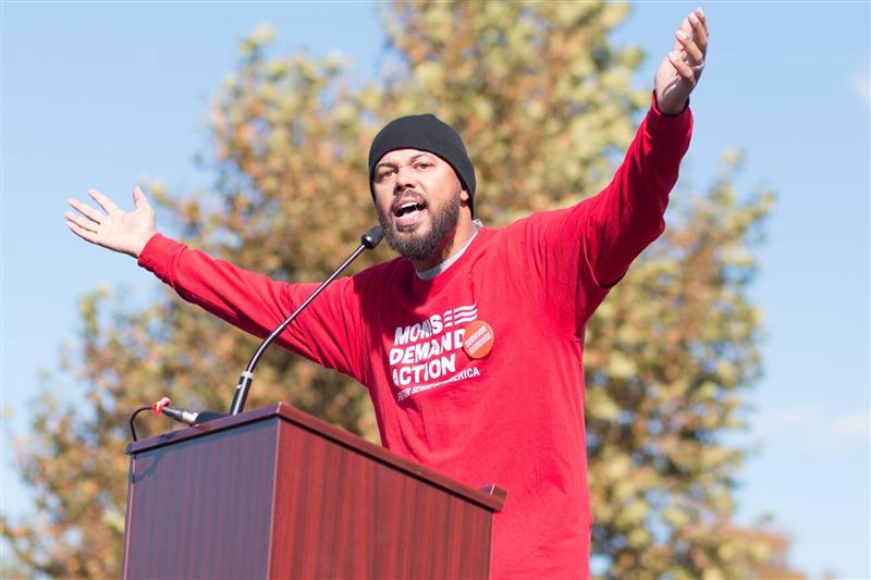 Khary Penebaker speaking at podium with arms wide at Moms Demand Action event