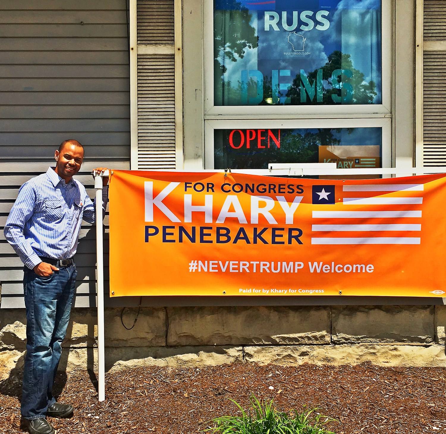 Khary Penebaker standing next to his Khary For Congress orange campaign banner