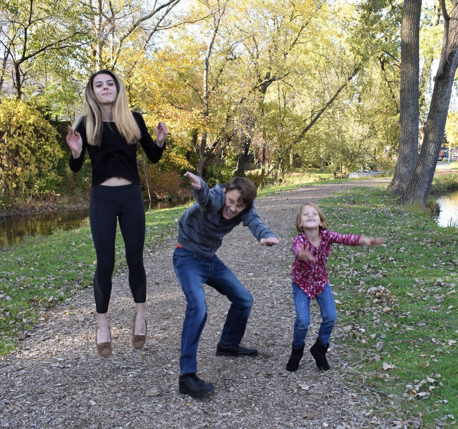 Khary's three children jumping on a wooded path